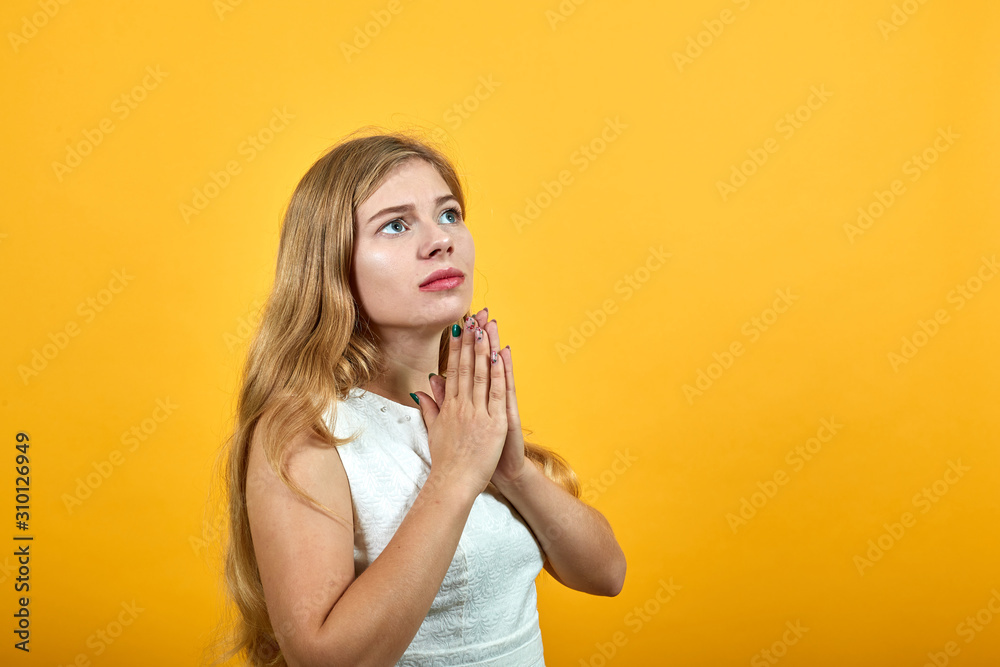 Charming caucasian young lady over isolated orange background wearing white shirt keeping hands over chin, looking up. Lifestyle concept Charming caucasian young lady over isolated orange background wearing white shirt keeping hands over chin, looking up. Lifestyle concept