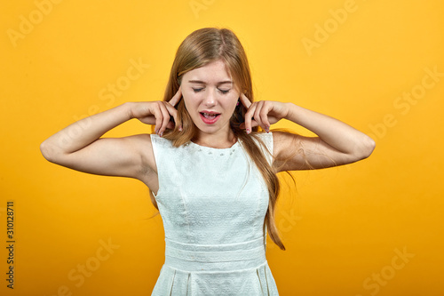 Attractive caucasian young woman keeping fingers on head, holding mouth opened, screaming, announcing over isolated orange background wearing white shirt. Lifestyle concept