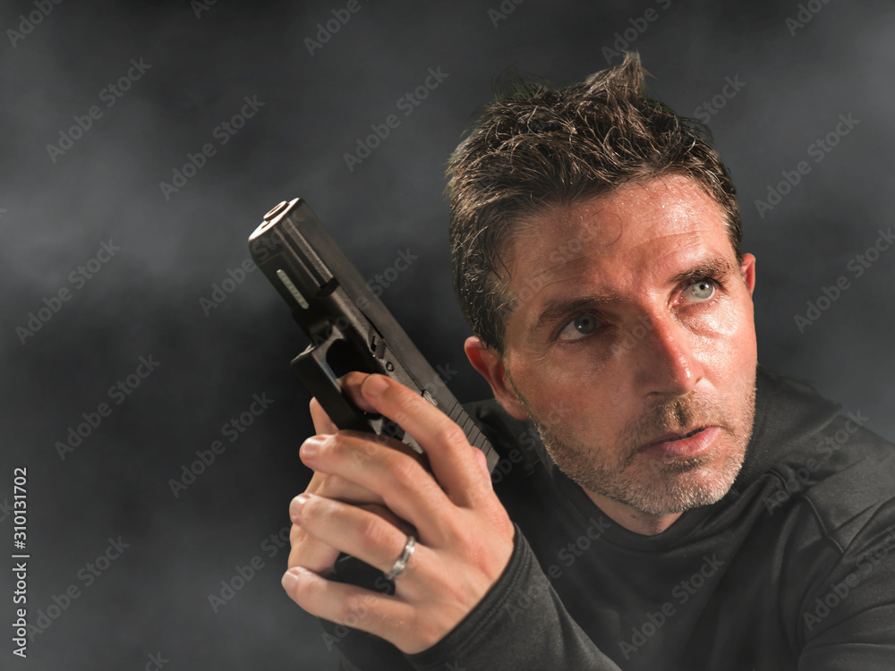 action portrait of serious and attractive hitman or special agent man holding gun pointing the handgun at cinematic edgy background in secret service movie Hollywood style