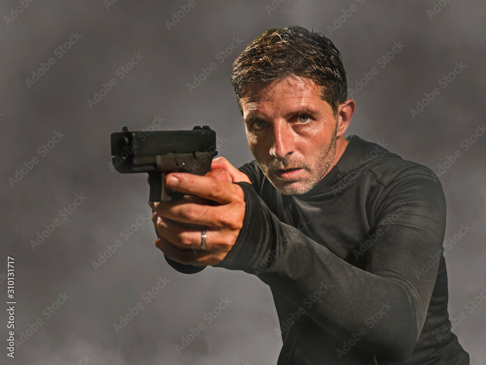 action portrait of serious and attractive hitman or special agent man holding gun pointing the handgun at cinematic edgy background in secret service movie Hollywood style action portrait of serious and attractive hitman or special agent man holding gun pointing the handgun at cinematic edgy background in secret service movie Hollywood style