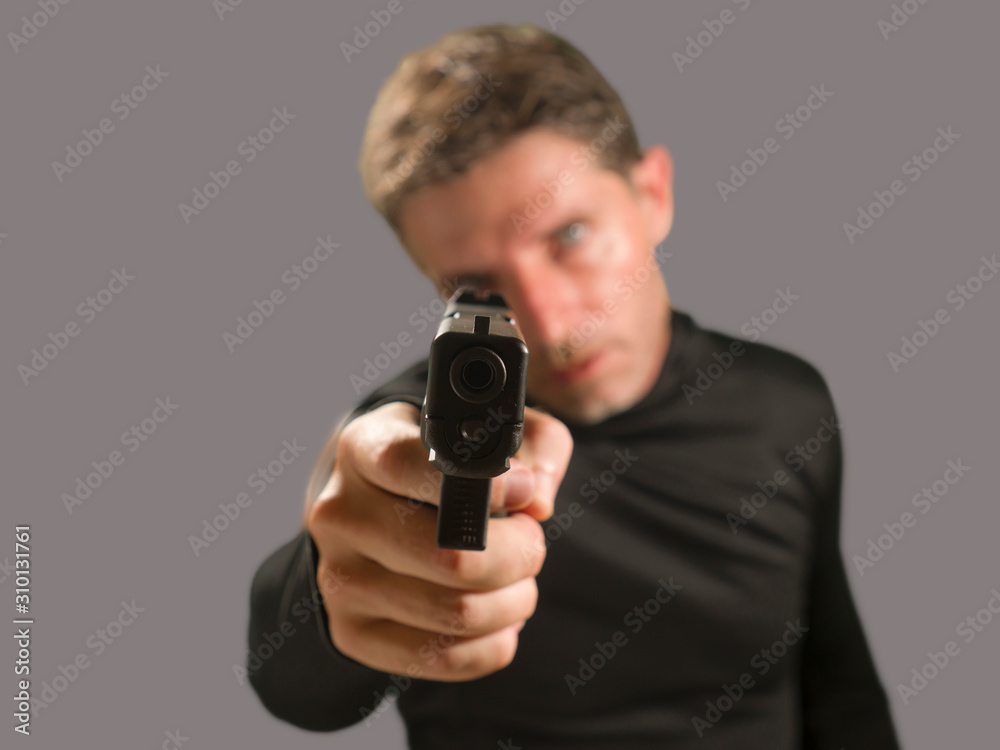 shallow depth of focus action portrait of serious and attractive hitman or special agent man holding gun pointing the handgun to the camera isolated on dark background shallow depth of focus action portrait of serious and attractive hitman or special agent man holding gun pointing the handgun to the camera isolated on dark background