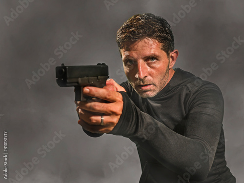 action portrait of serious and attractive hitman or special agent man holding gun pointing the handgun at cinematic edgy background in secret service movie Hollywood style