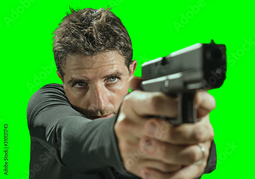 chroma key green background action portrait of serious and attractive hitman or special agent man holding gun pointing the handgun on cinematic light in secret service movie style