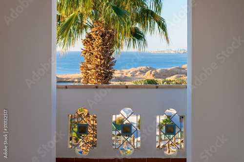 Balcony with a view of the blue sea. Tall palm tree next to the bolcony at the sea resort. View of a hot seaside resort. photo