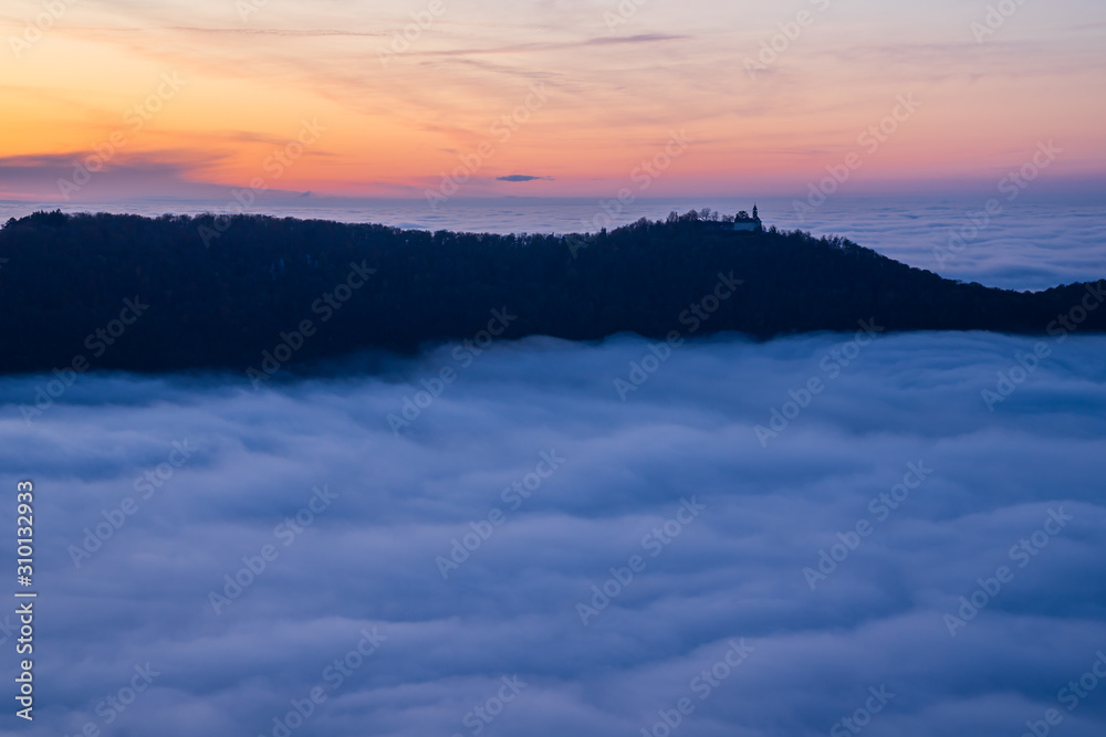 Germany, Magical aerial view above fog clouds in valley of swabian jura nature landscape at sunset with orange sky near stuttgart with view to castle teck