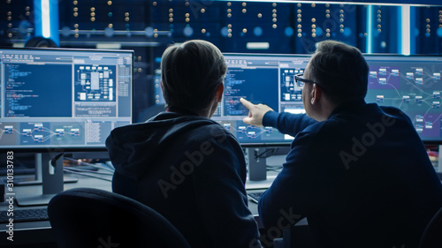 Two Professional IT Programers Discussing Blockchain Data Network Architecture Design and Development Shown on Desktop Computer Display. Working Data Center Technical Department with Server Racks 