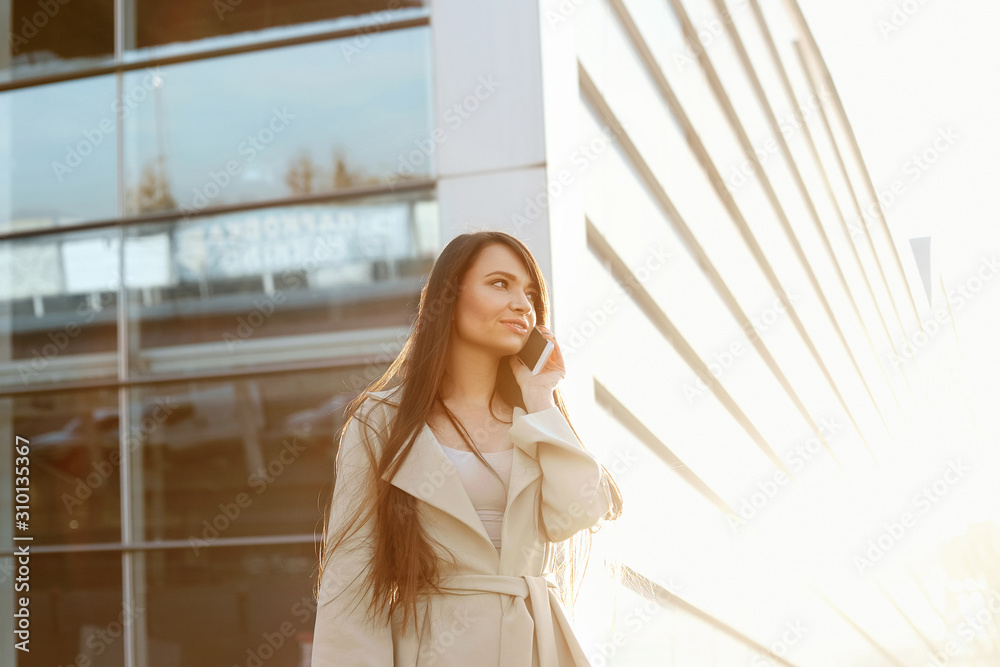Fototapeta premium Business woman with the phone near office. Portrait of beautiful smiling female with phone, standing outdoors. Phone communication.