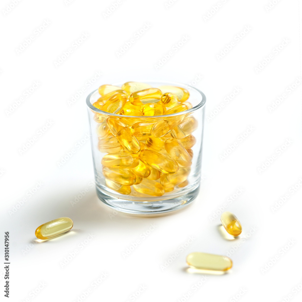 Yellow translucent pills in a glass Cup on a white background. Isolate. Omega, vitamins, food supplements. Yellow translucent pills in a glass Cup on a white background. Isolate. Omega, vitamins, food supplements.