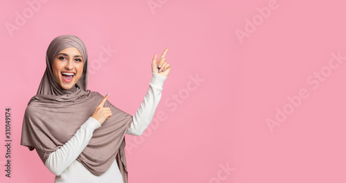 Cheerful muslim woman pointing at copy space on pink background