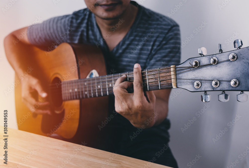 Obraz premium Man wearing a striped shirt playing guitar in his room with romantic atmosphere full of symphonic music.