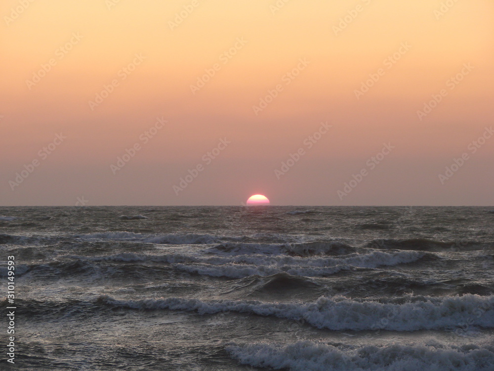 The stormy sea pushes a bright solar disk to the surface against a red-orange sky.