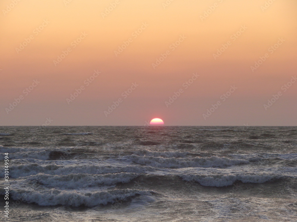 The stormy sea pushes a bright solar disk to the surface against a red-orange sky.