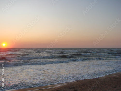 Morning storm waves of the Azov Sea covered with foam against the background of rainbow colors of sunrise.