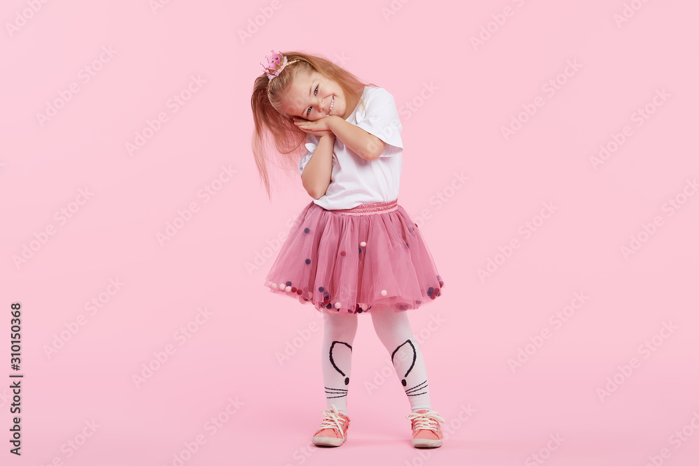 Φωτογραφία A cheerful little girl with in a tulle skirt and princess crown on her head isolated on a pink background
