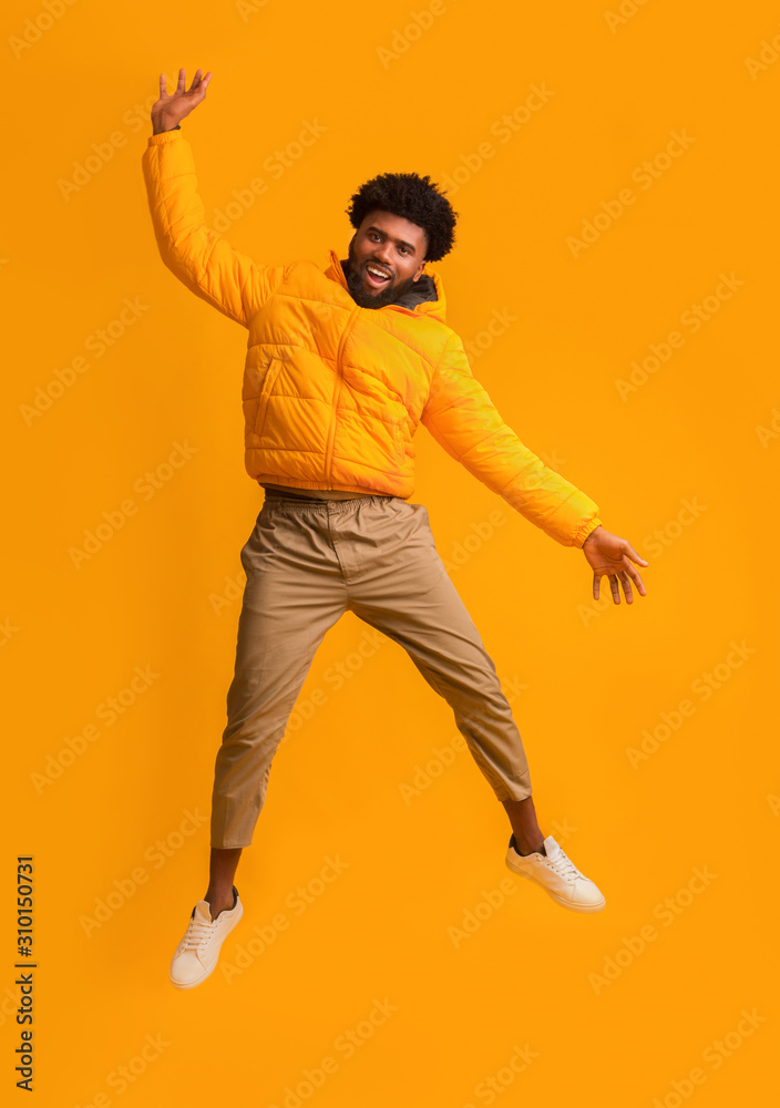Joyful black man in winter jacket happily jumping up Joyful black man in winter jacket happily jumping up