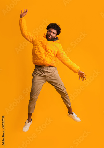 Joyful black man in winter jacket happily jumping up