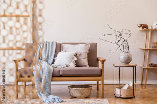 Stylish interior of living room at cozy apartment with brown wooden sofa, coffe table, bookstand , pillow, plaid and elegant accessories. Beige and japandi concept. Modern home staging. Template. photo