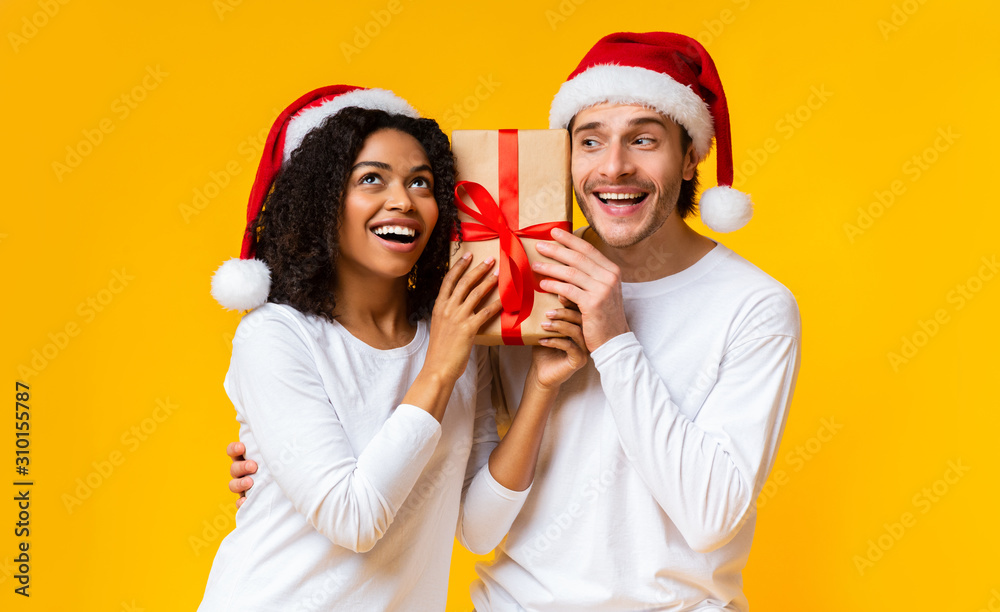 Portrait of happy couple holding gift box and wearing santa hats