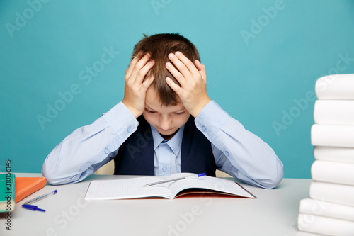 Frustrated upset boy at school sitting at the desk and dotng classwork