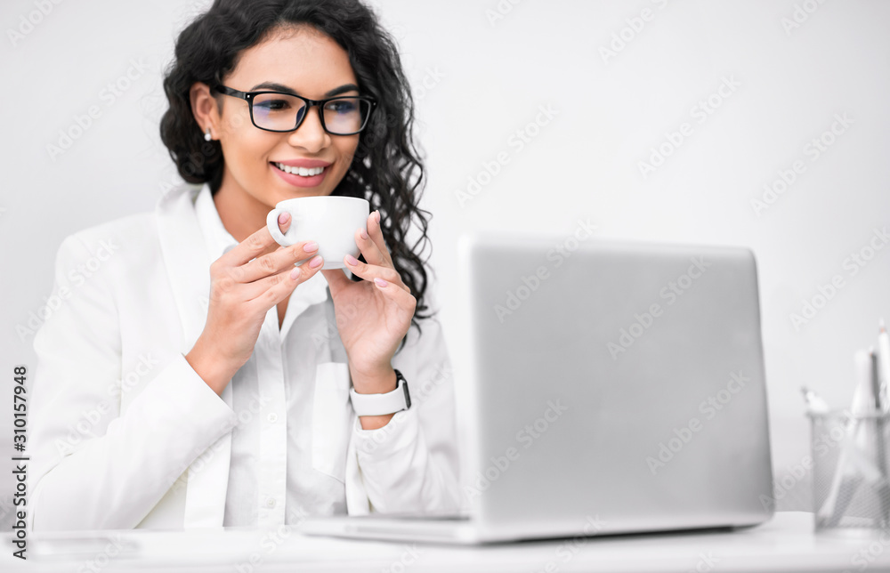 Mexican girl holding cup of cofee working on laptop Mexican girl holding cup of cofee working on laptop