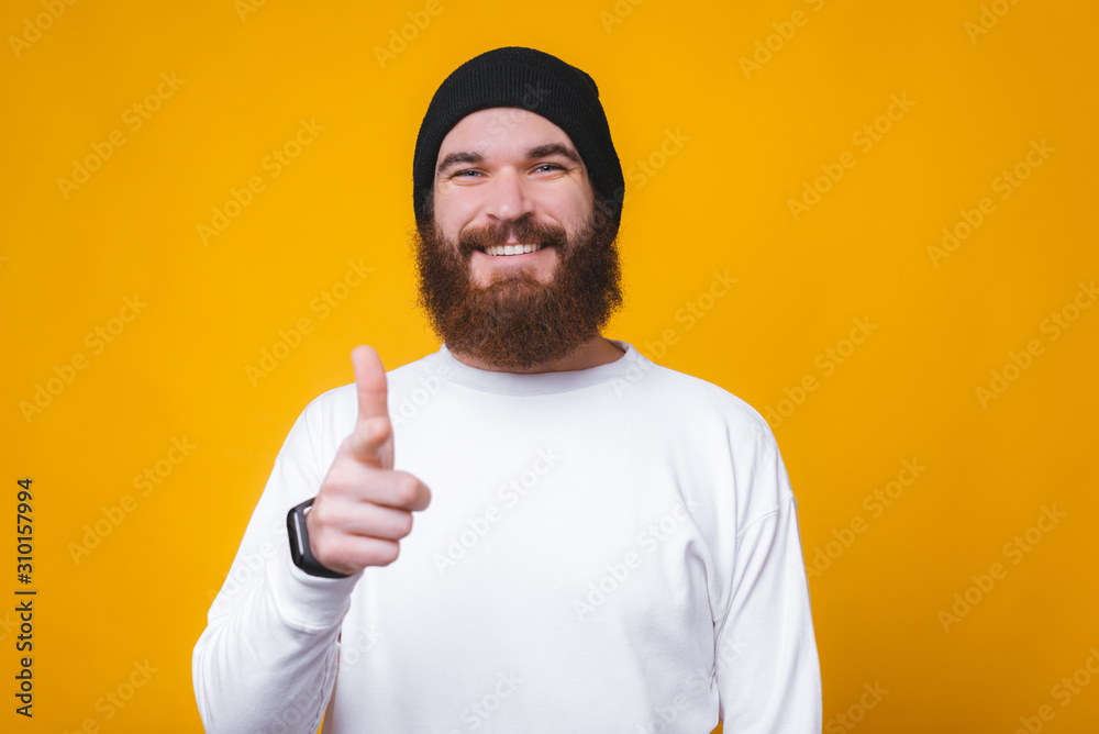 Cheerful young man with beard standing over yellow background and pointing at the camera Cheerful young man with beard standing over yellow background and pointing at the camera
