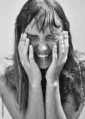woman laughing whilst being splashed by water. Female holding her face whilst smiling. Black and white portrait of female model laughing.