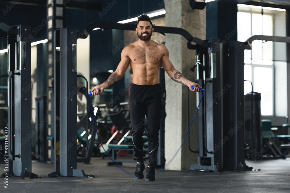 Shirtless muscular guy jumping with skipping rope in gym Shirtless muscular guy jumping with skipping rope in gym