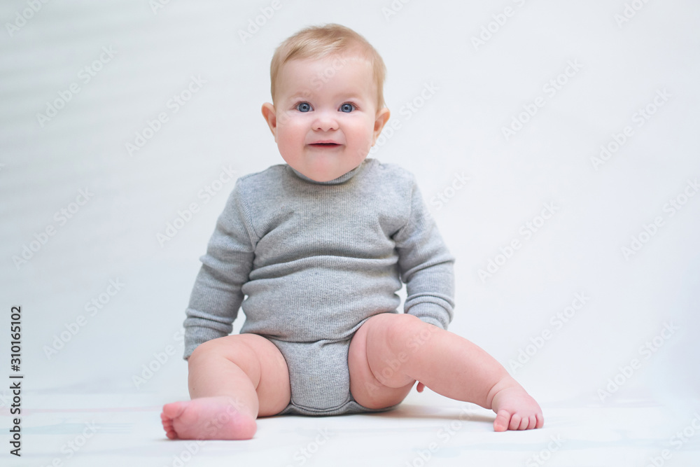 A 6 month old baby learns to sit down. photo on a neutral background A 6 month old baby learns to sit down. photo on a neutral background