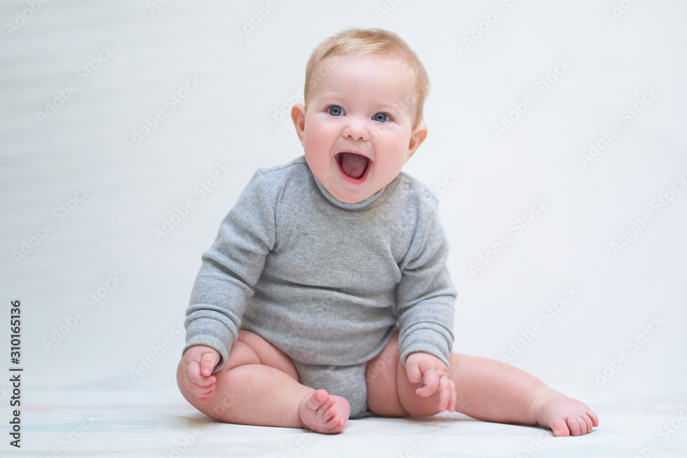 A 6 month old baby learns to sit down. photo on a neutral background A 6 month old baby learns to sit down. photo on a neutral background