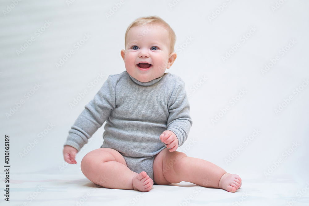 A 6 month old baby learns to sit down. photo on a neutral background A 6 month old baby learns to sit down. photo on a neutral background
