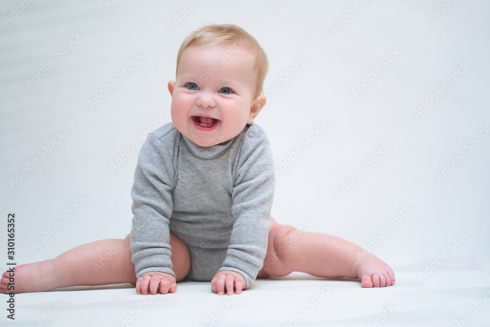 A 6 month old baby learns to sit down. photo on a neutral background A 6 month old baby learns to sit down. photo on a neutral background