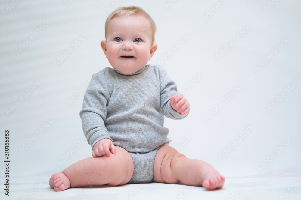 A 6 month old baby learns to sit down. photo on a neutral background A 6 month old baby learns to sit down. photo on a neutral background