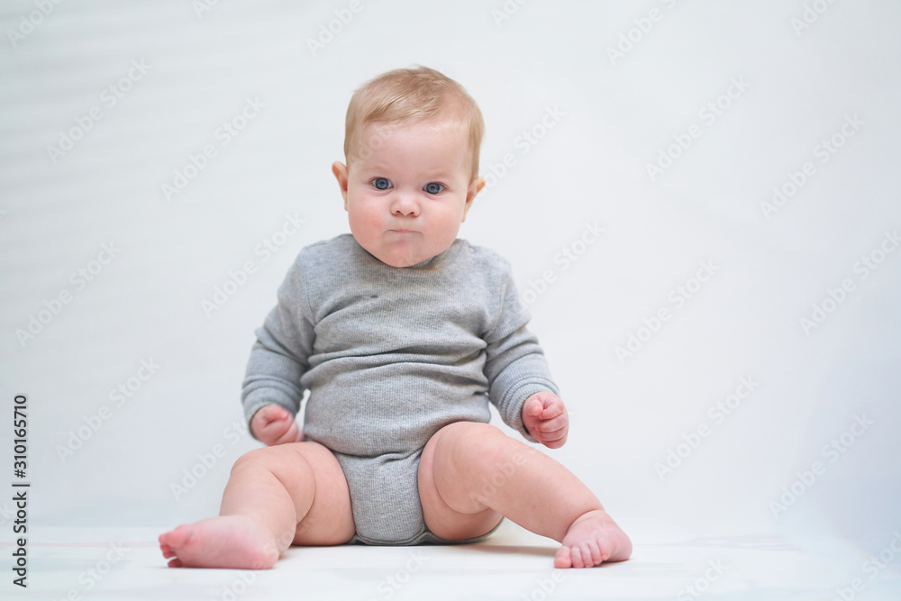 A 6 month old baby learns to sit down. photo on a neutral background A 6 month old baby learns to sit down. photo on a neutral background