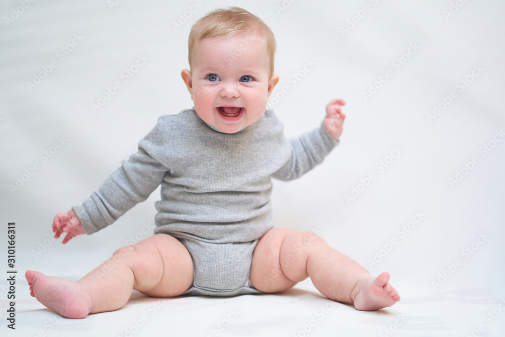A 6 month old baby learns to sit down. photo on a neutral background A 6 month old baby learns to sit down. photo on a neutral background