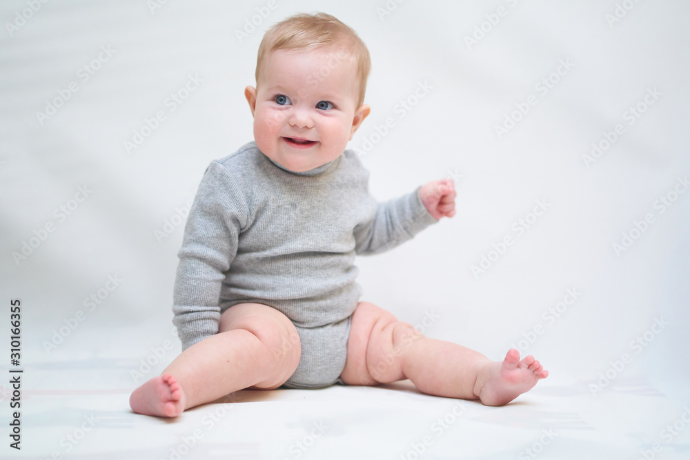 A 6 month old baby learns to sit down. photo on a neutral background A 6 month old baby learns to sit down. photo on a neutral background