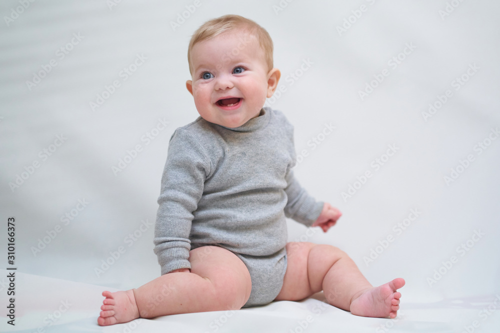 A 6 month old baby learns to sit down. photo on a neutral background A 6 month old baby learns to sit down. photo on a neutral background