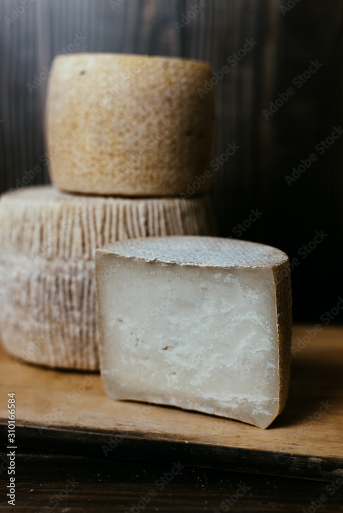 Different homemade cheeses on a dark wooden background. Pieces and cheese heads of kravot, manchego, Paramezan. Goat and cow cheese on baking paper. Handwork. Close up Different homemade cheeses on a dark wooden background. Pieces and cheese heads of kravot, manchego, Paramezan. Goat and cow cheese on baking paper. Handwork. Close up