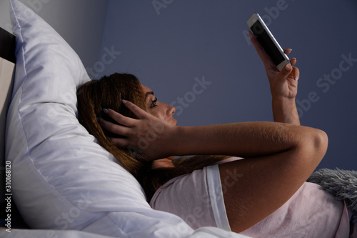 Young woman using phone at night in the bed at home. Insomnia concept
