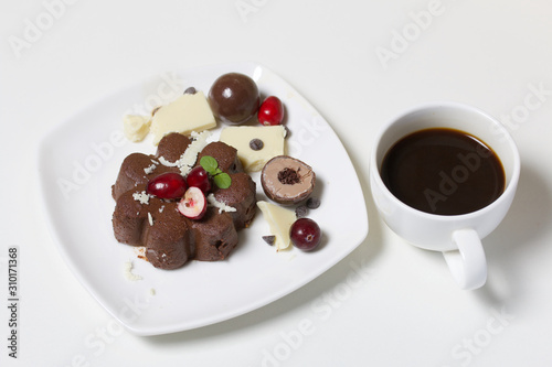 Chocolate fudge garnished with chocolate  mint and cranberries. Lies on a white plate  on a white background. Near a cup of coffee.