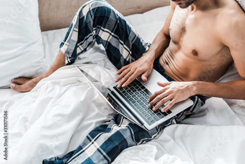 cropped view of sexy bi-racial man using laptop in morning