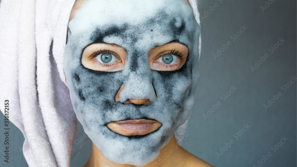Bubble charcoal oxygen face mask. Beautiful young woman with bubbling carbonated mask and towel on the head. Face treatment.