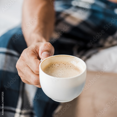 cropped view of bi-racial man holding cup of coffee in morning