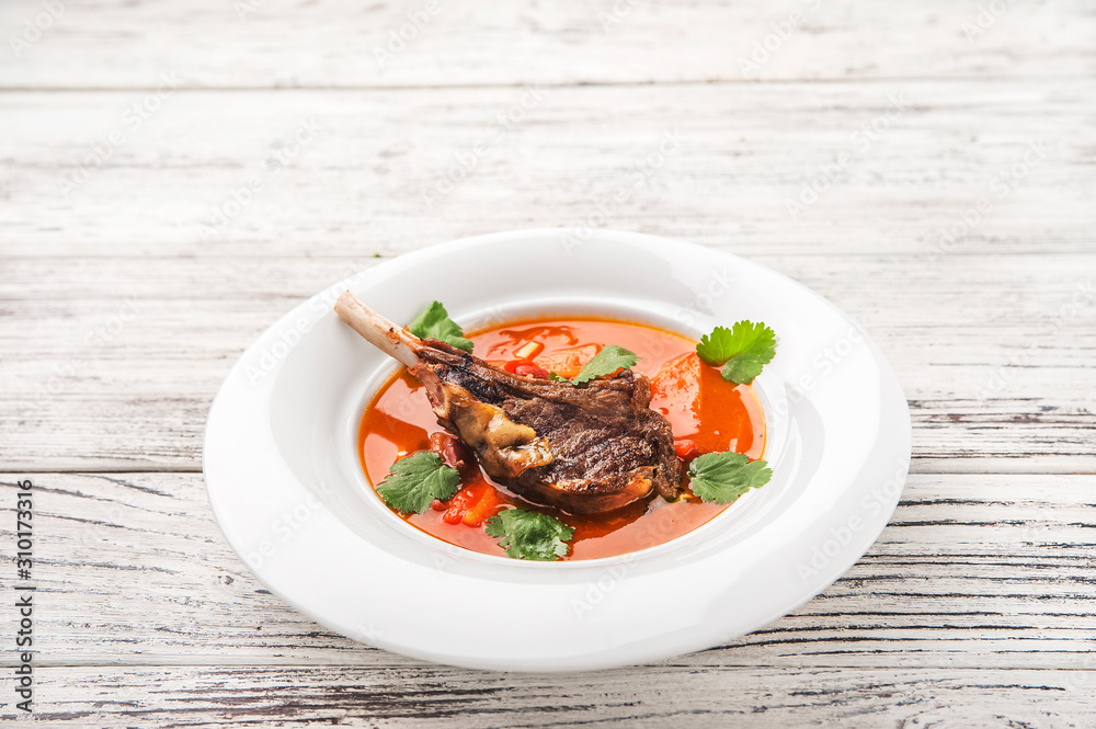 Vegetable soup with tomatoes in a restaurant close-up. Lamb soup on bone noodles on a white plate and copy space. Vegetable soup with tomatoes in a restaurant close-up. Lamb soup on bone noodles on a white plate and copy space.