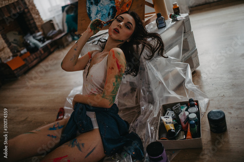 The artist sits on floor in an art workshop in a creative mess.
