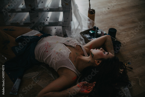 The artist lies on floor in an art workshop among a creative mess.