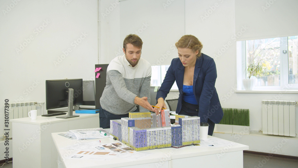 Engineers look at scheme and arrange models of houses on the table Engineers look at scheme and arrange models of houses on the table