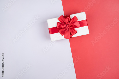 Beautiful gift box with a red bow on a red and gray background. Space for text