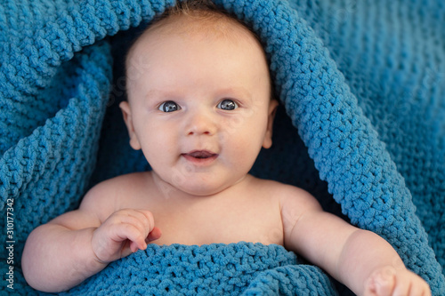 A cute baby boy wrapped in a cosy blue blanket looking at the camera