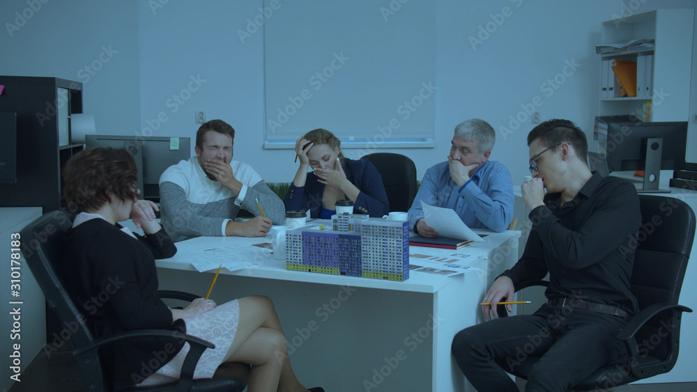 Fototapeta premium Tired engineers sit at a table and yawn