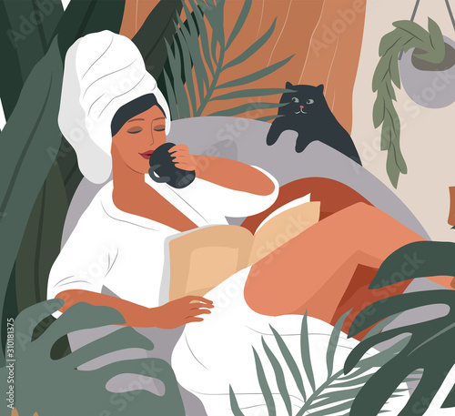 Happy cute girl with towel on head and in bathrobe, drinks coffeeor tea in morning after bathing, read the newspaper and resting with cat. Feminine Daily life by young woman with